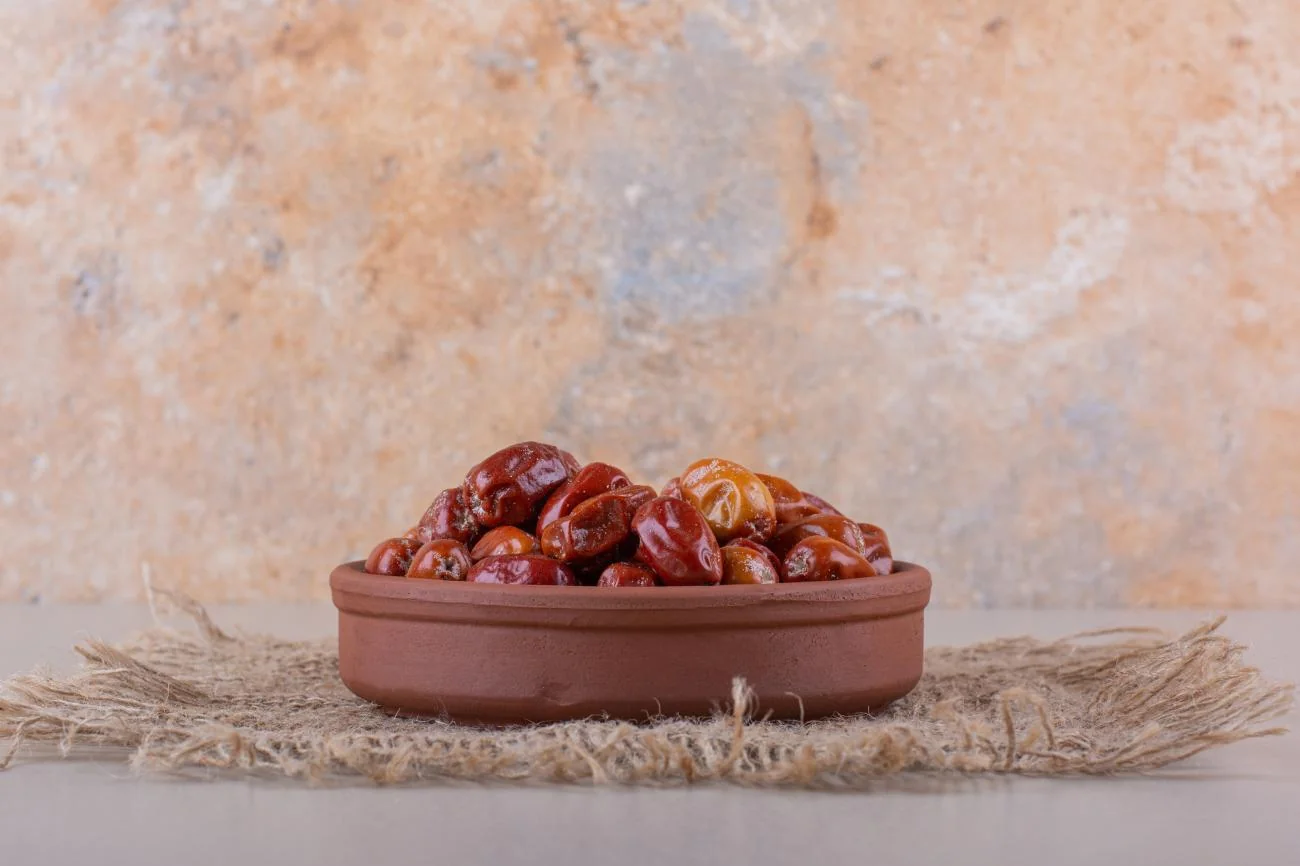 A clay bowl of dates on a woven mat